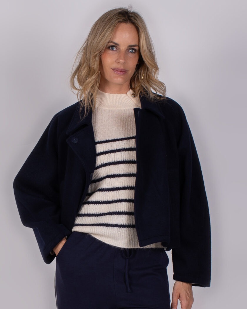 Vrouw draagt een donkerblauwe jas over een crèmekleurige trui met donkerblauwe strepen uit de Studio AW25-26 collectie.