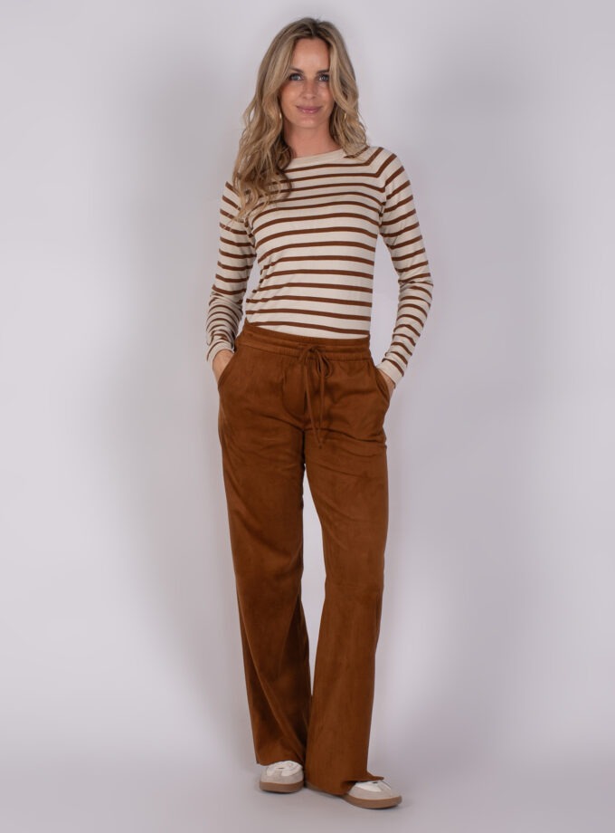 Vrouw draagt een beige en bruin gestreepte top met losse, bruine broek en lichte sneakers.
