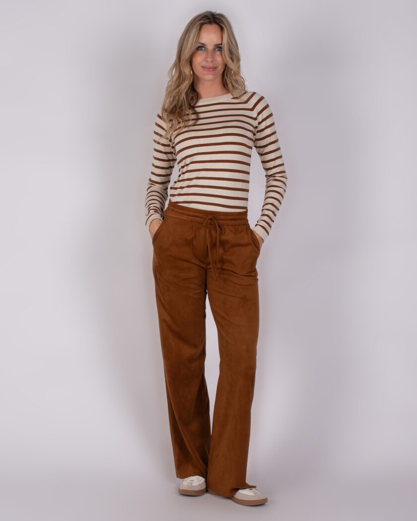 Vrouw draagt een beige en bruin gestreepte top met losse, bruine broek en lichte sneakers.