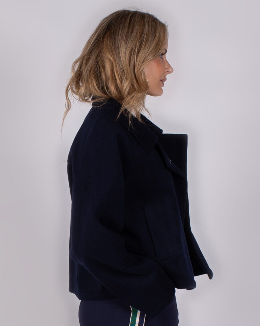 Vrouw in zijaanzicht draagt een donkerblauw jack uit de Studio AW25-26-collectie.