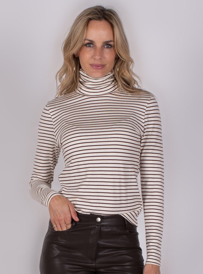 Vrouw draagt een gestreepte coltrui en zwarte leren broek uit de Studio_AW25-26-61 collectie.