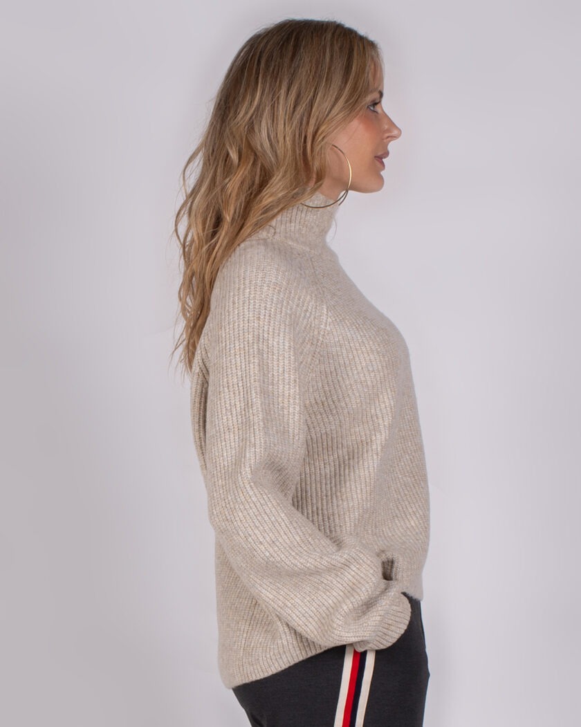 Vrouw in profiel draagt een beige ribgebreide coltrui en een donker sportief broekje met rood-witte strepen.