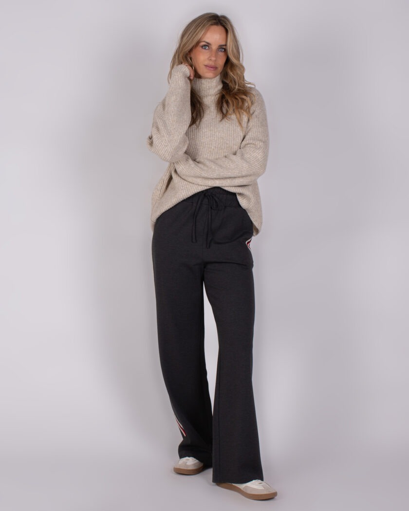Vrouw draagt een beige coltrui en donkergrijze wijde broek met sportieve sneakers uit de Studio AW25-26 collectie.