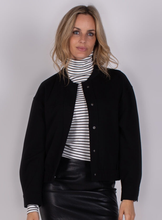 Vrouw draagt een zwart jack over een gestreepte coltrui en een zwarte leren rok uit de Studio AW25-26 collectie.