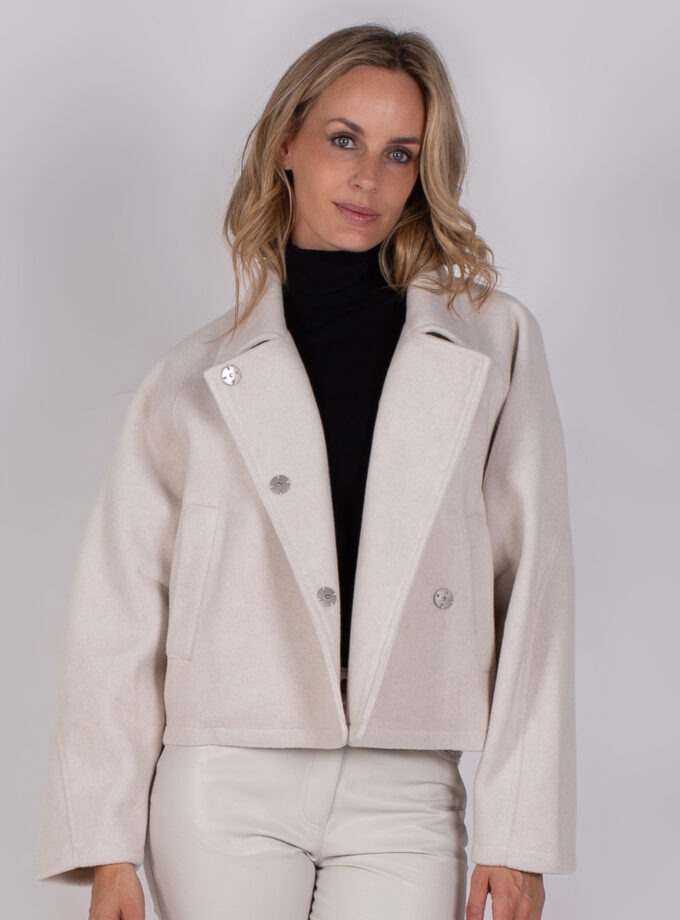 Vrouw draagt een lichtbeige, wollen korte jas met grote revers en zilverkleurige knopen uit de Studio AW25-26 collectie.