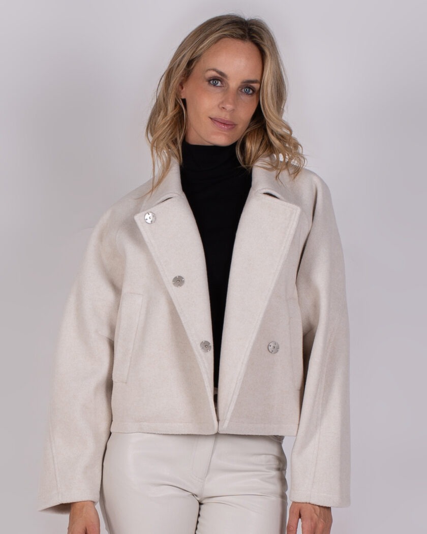 Vrouw draagt een lichtbeige, wollen korte jas met grote revers en zilverkleurige knopen uit de Studio AW25-26 collectie.