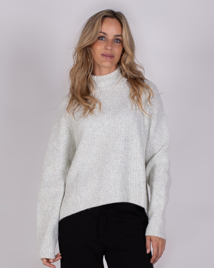 Vrouw draagt een lichtgrijze, geribde trui met col en zwarte broek uit de Studio AW25-26 collectie.