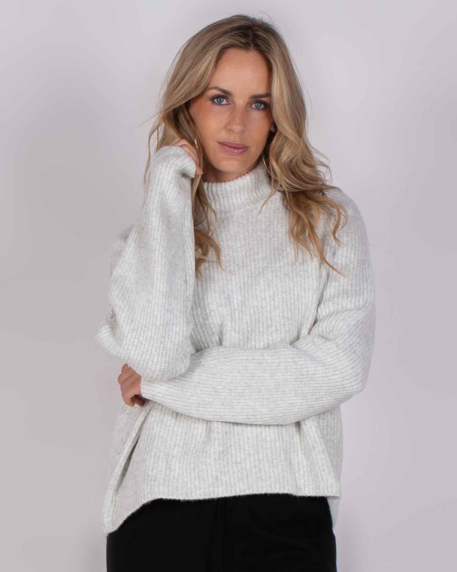 Vrouw draagt een lichtgrijze, ribgebreide trui met col uit de Studio AW25-26 collectie.