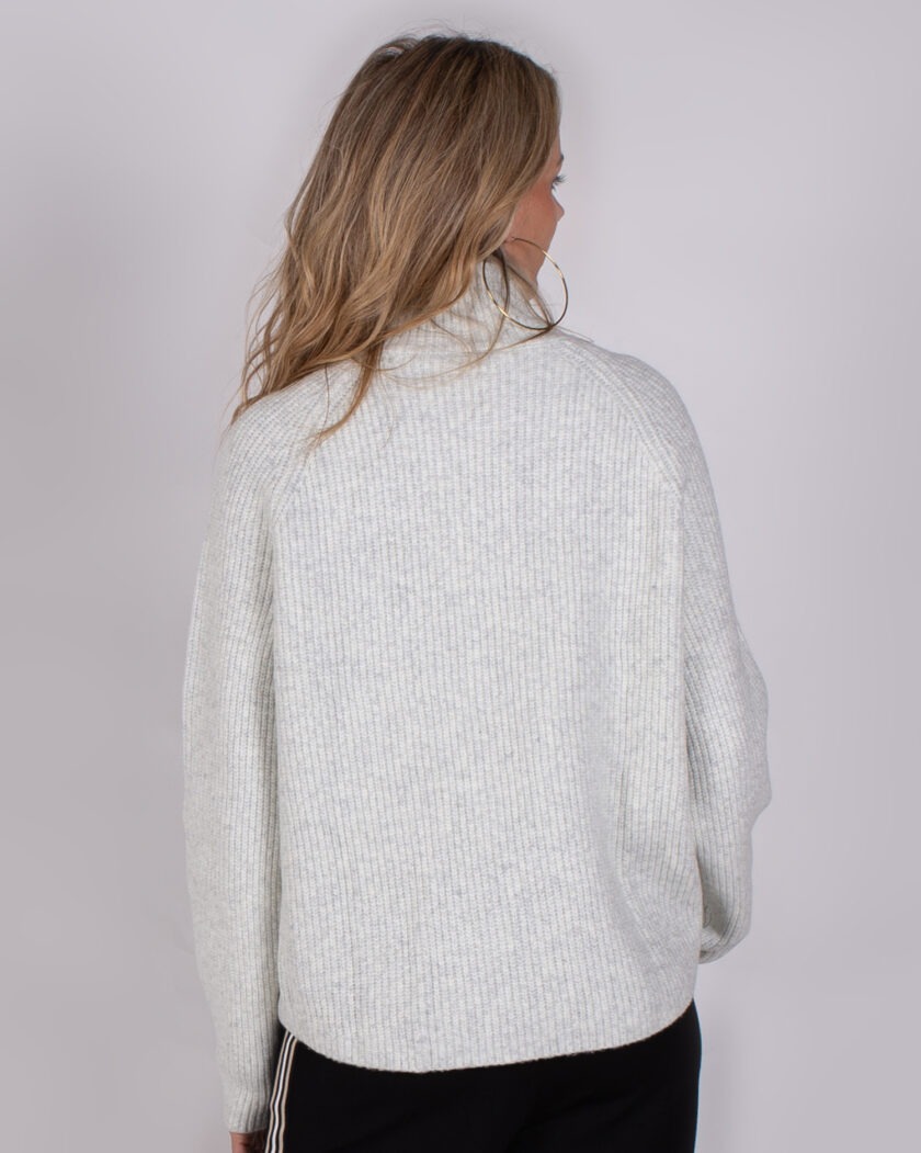 Achteraanzicht van een vrouw met los haar die een lichtgrijze, geribde trui met col draagt uit de Studio AW25-26 collectie.