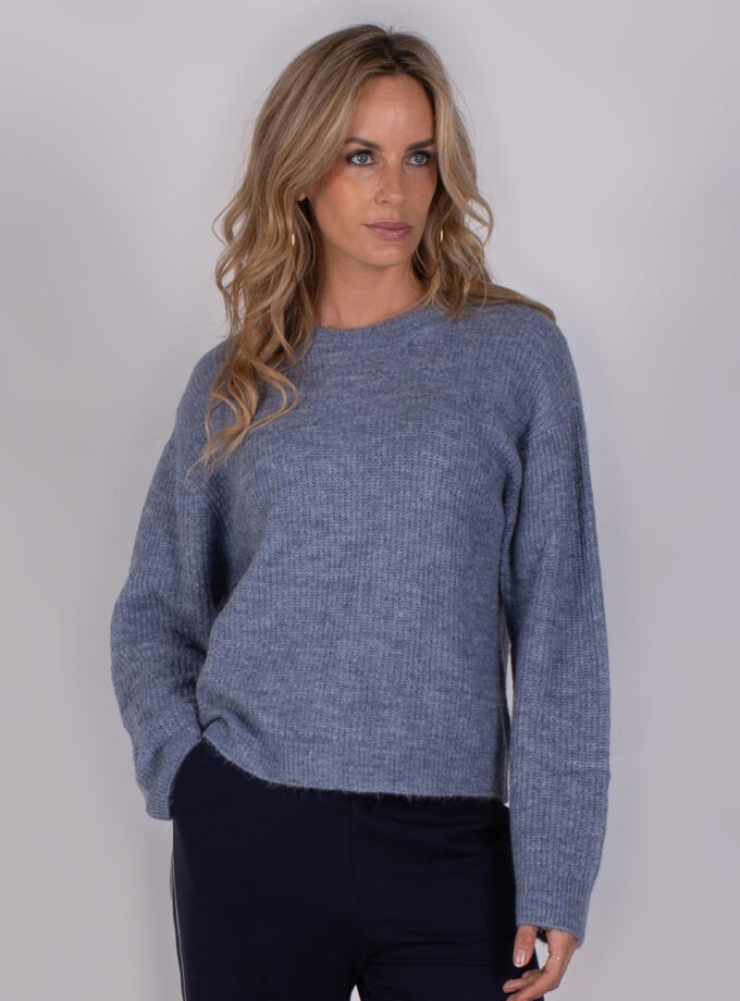 Vrouw poseert in een blauwgrijze gebreide trui uit de Studio AW25-26 collectie.