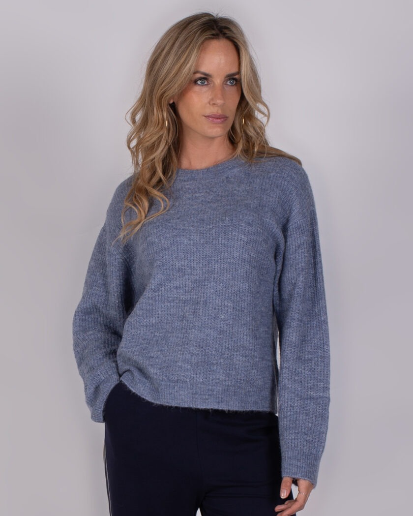 Vrouw poseert in een blauwgrijze gebreide trui uit de Studio AW25-26 collectie.