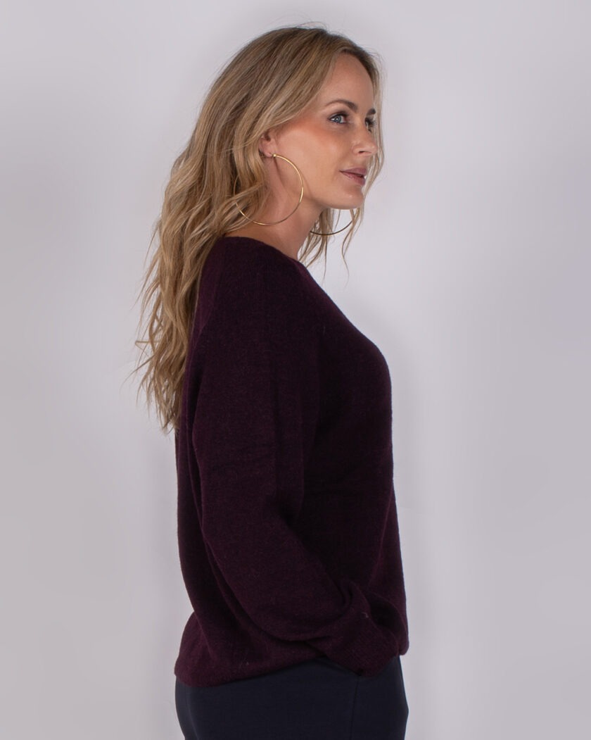 Model in zijaanzicht draagt een donkerpaarse trui uit de Studio AW25-26 collectie.