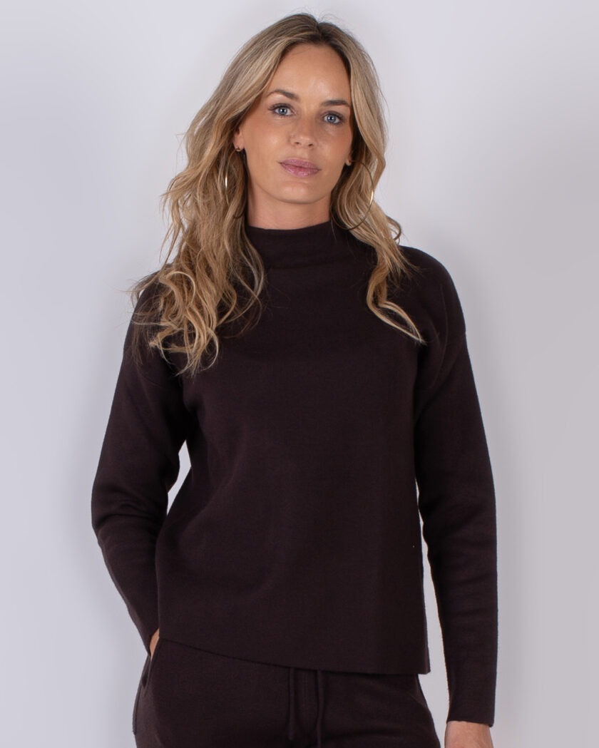 Vrouw draagt een donkerbruine coltrui en bijpassende broek uit de Studio AW25-26 collectie.