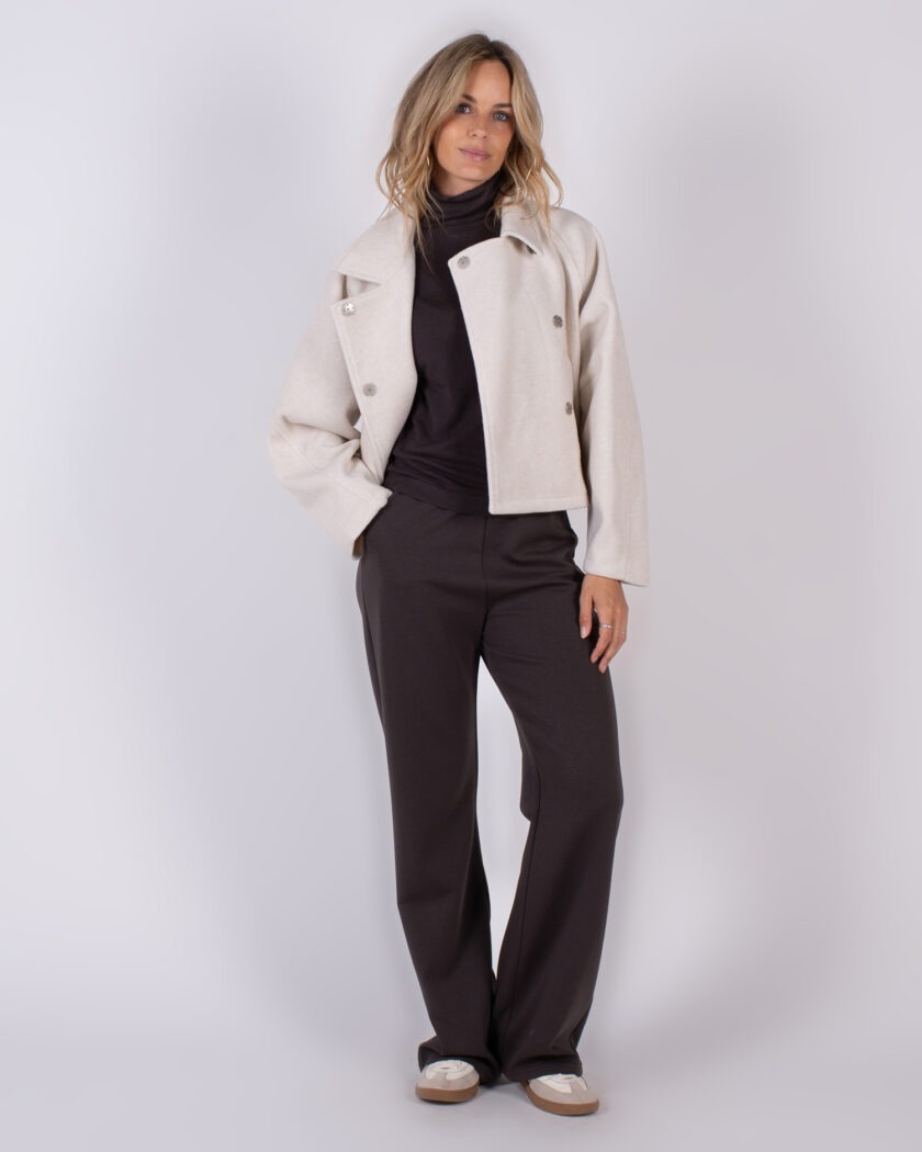 Vrouw in studio-outfit AW25-26 met een beige cropped jas, donkere coltrui en donkerbruine broek.