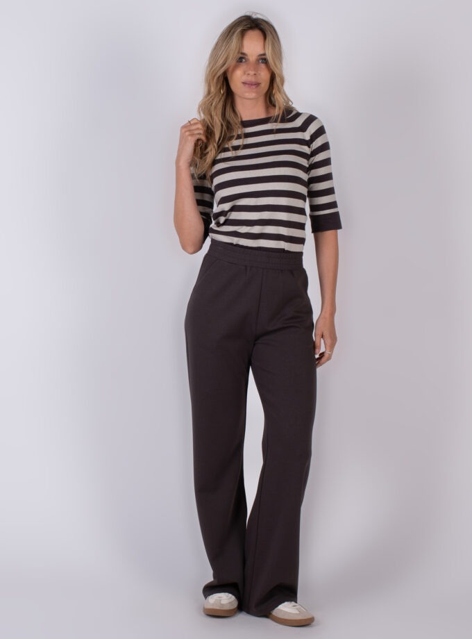 Vrouw draagt een gestreepte top met half lange mouwen en donkerbruine, losvallende broek uit de Studio AW25-26 collectie.