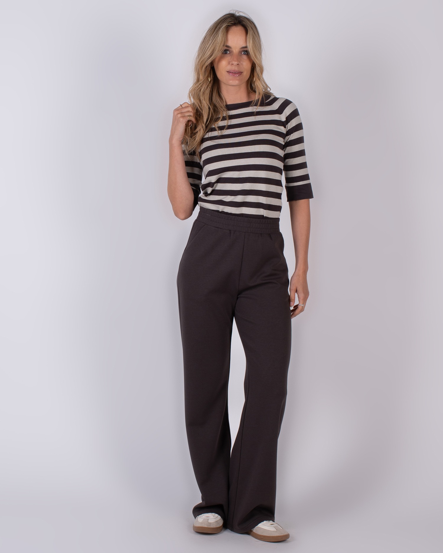 Vrouw draagt een gestreepte top met half lange mouwen en donkerbruine, losvallende broek uit de Studio AW25-26 collectie.