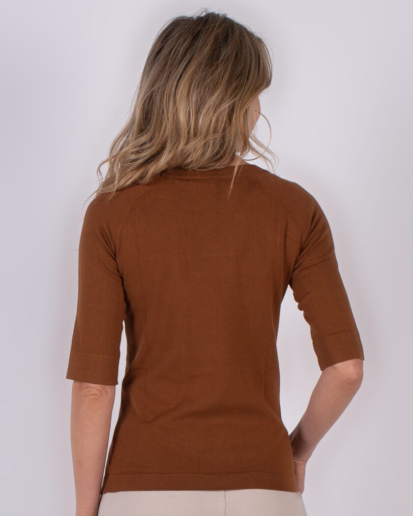 Vrouw met halflang blond haar draagt een bruin shirt met halve mouwen, gezien van achteren.