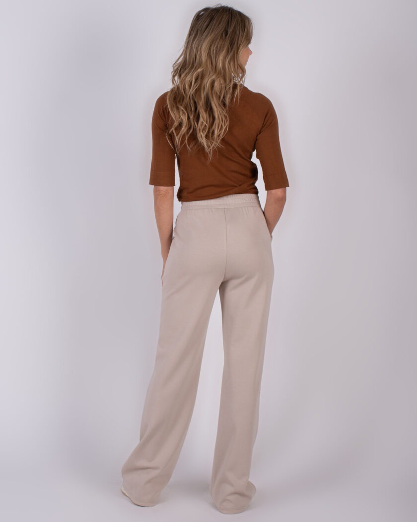 Vrouw van achteren in een bruine top met driekwartmouwen en beige, wijde broek.