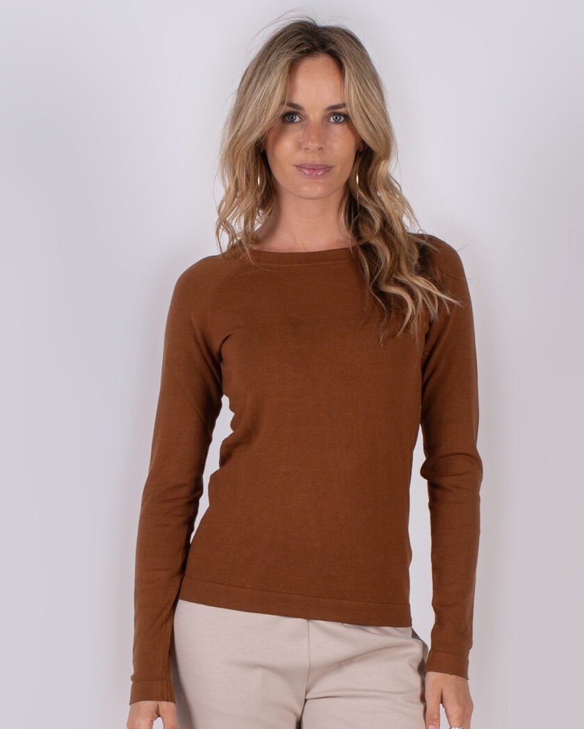 Vrouw draagt een bruin, lang mouwshirt uit de Studio AW25-26 collectie tegen een neutrale achtergrond.