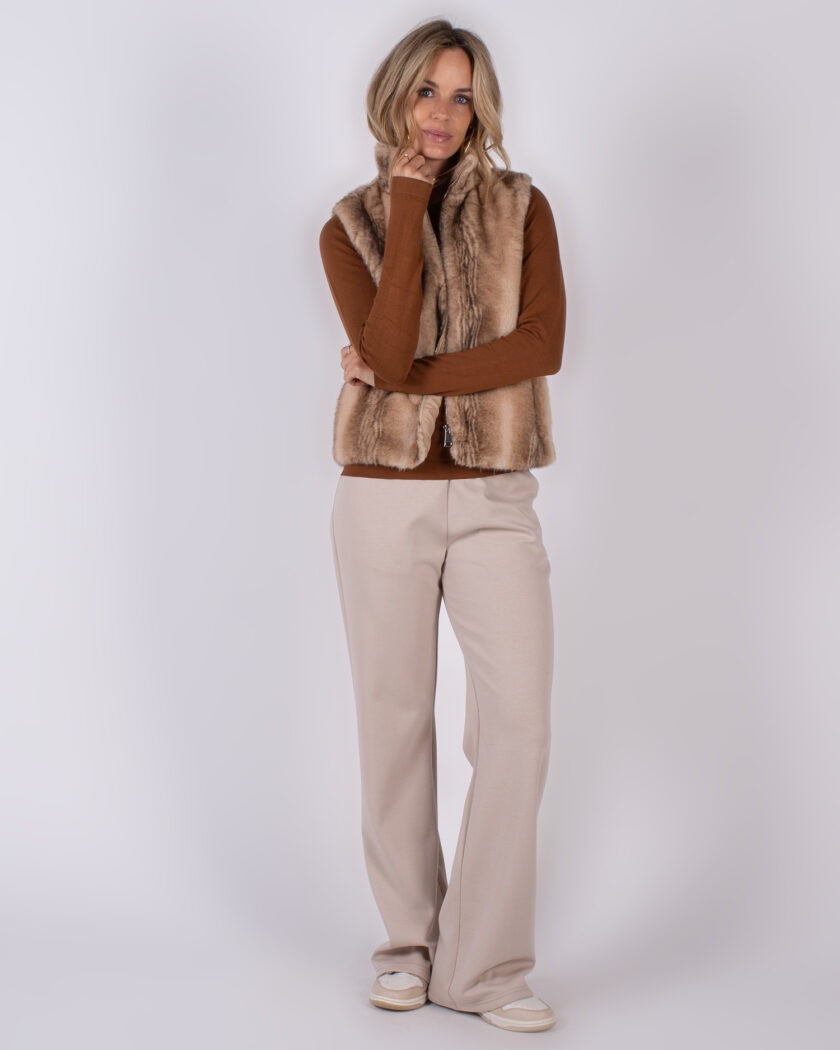 Vrouw poseert in beige wide-leg broek, bruine trui en lichtbruin faux fur gilet uit de Studio AW25-26 collectie.