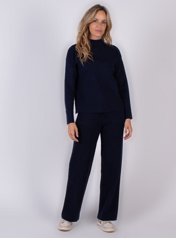 Vrouw draagt een donkerblauwe loungset met lange mouwen en losse broek uit de Studio AW25-26 collectie.