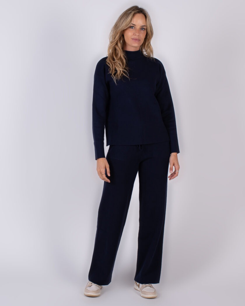 Vrouw draagt een donkerblauwe loungset met lange mouwen en losse broek uit de Studio AW25-26 collectie.