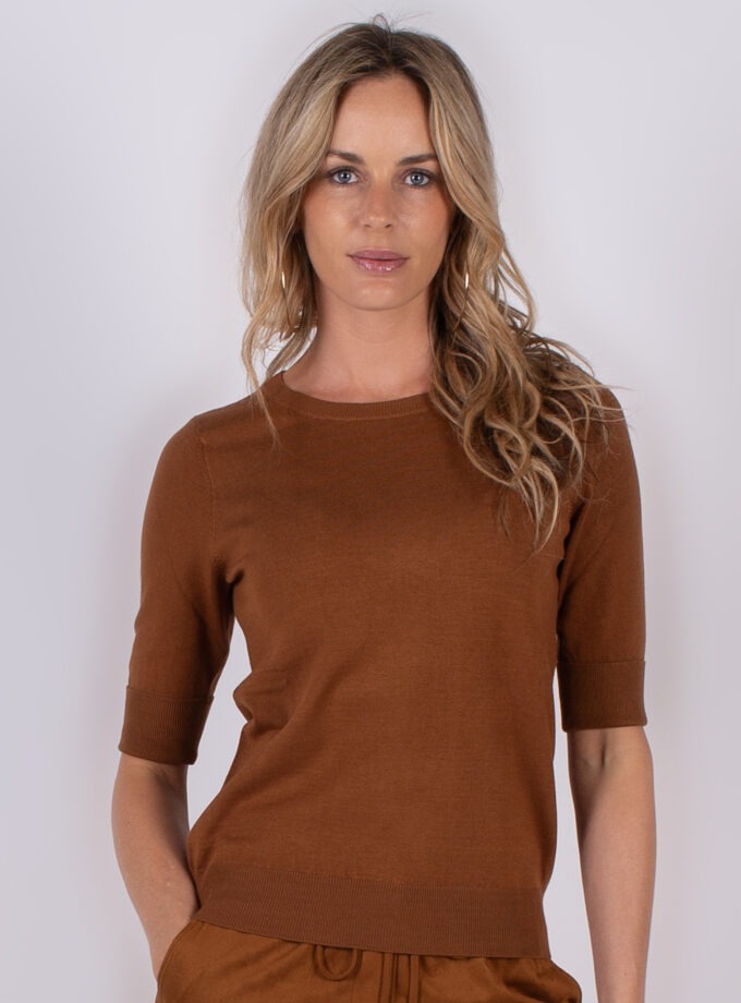 Vrouw poseert in een bruin, half-mouw gebreid shirt uit de Studio AW25-26 collectie.