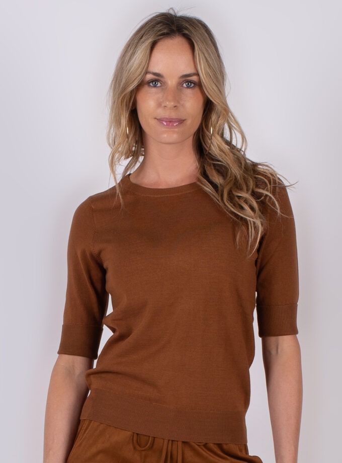 Vrouw draagt een bruin, half mouwloos truitje uit de Studio AW25-26 collectie tegen een neutrale achtergrond.