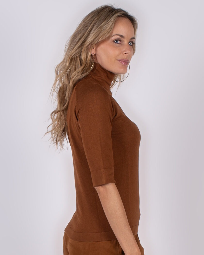 Vrouw in zijaanzicht draagt een bruine coltrui met driekwartmouwen uit de Studio AW25-26 collectie.