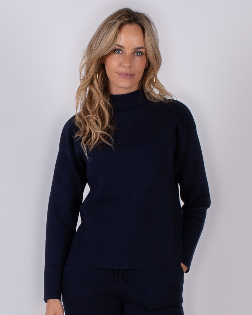 Vrouw poseert in een donkerblauwe trui en matchende broek uit de Studio AW25-26 collectie.