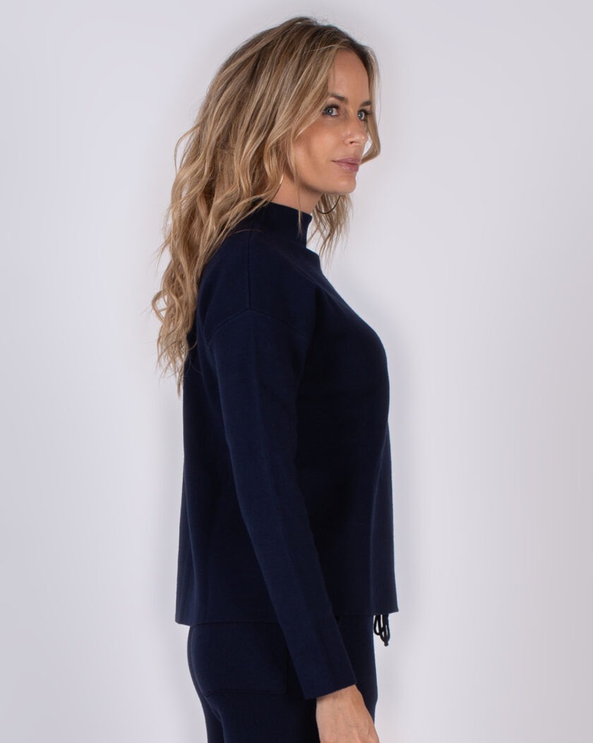 Vrouw in profiel draagt een donkerblauwe trui met lange mouwen uit de Studio AW25-26 collectie.