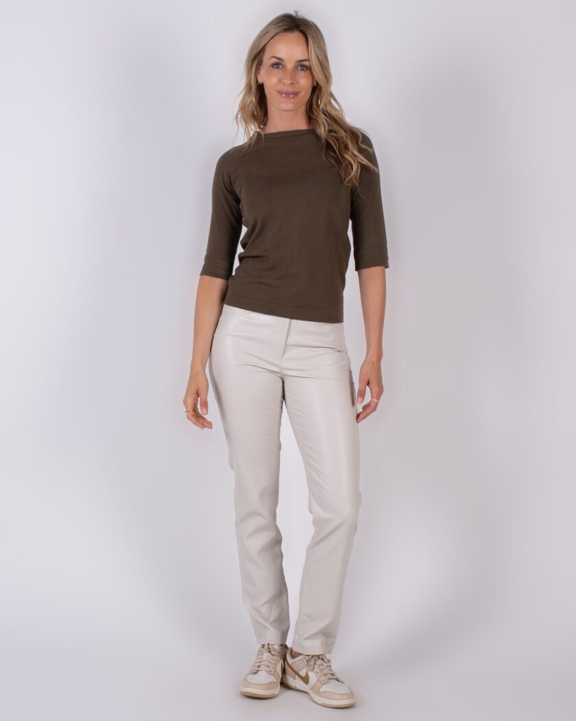 Vrouw draagt een donkergroene top met driekwartsmouwen en een lichtgekleurde broek uit de Studio AW25-26 collectie.
