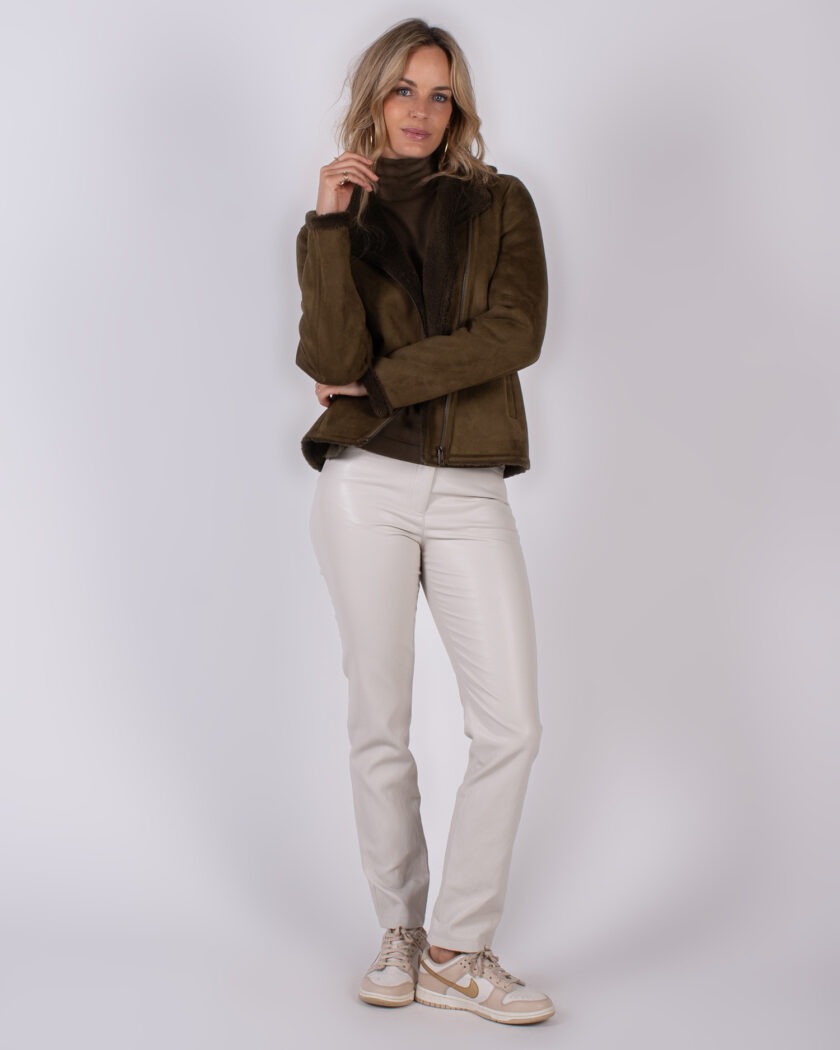 Vrouw in een Studio_AW25-26 outfit met een donkergroene shearling jas, coltrui, lichtbeige broek en beige sneakers.