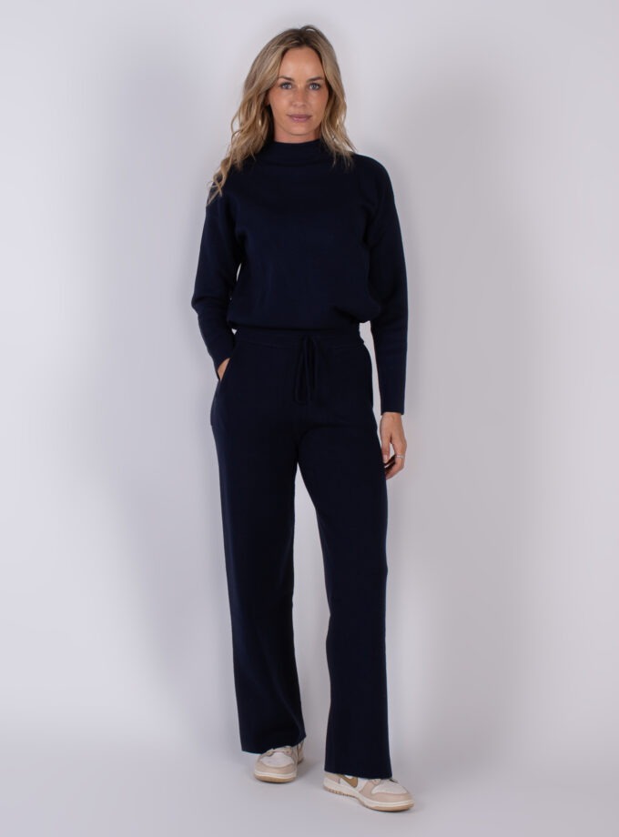 Vrouw draagt een donkerblauwe lounge-set met coltrui en wijde broek uit de Studio AW25-26 collectie.