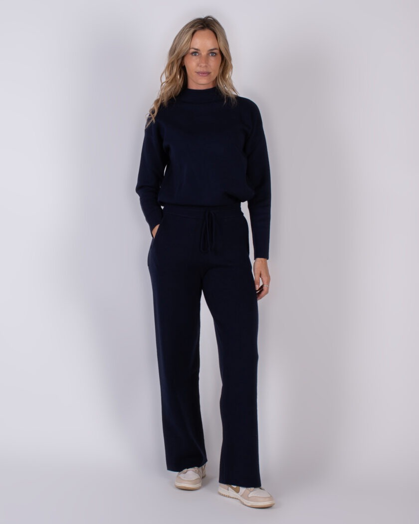 Vrouw draagt een donkerblauwe lounge-set met coltrui en wijde broek uit de Studio AW25-26 collectie.