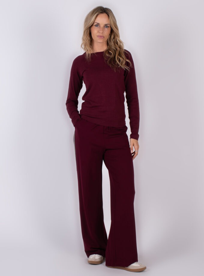 Vrouw draagt een bordeauxrode lounge-set met lange mouwen en wijde broek in studio-opstelling.