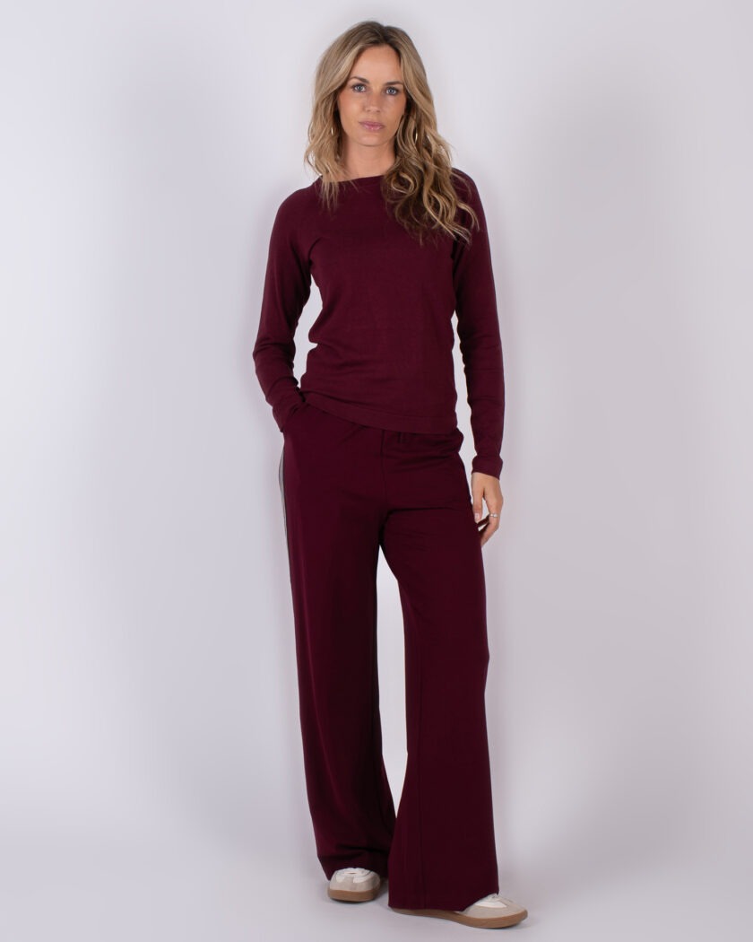 Vrouw draagt een bordeauxrode lounge-set met lange mouwen en wijde broek in studio-opstelling.