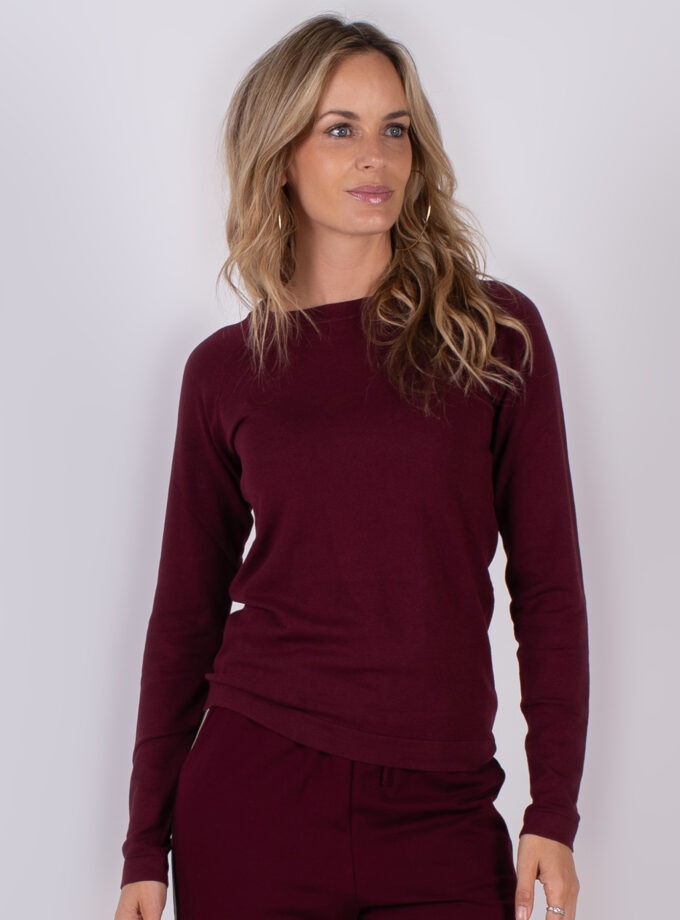 Vrouw draagt een bordeauxrode trui met bijpassende broek uit Studio AW25-26 collectie.