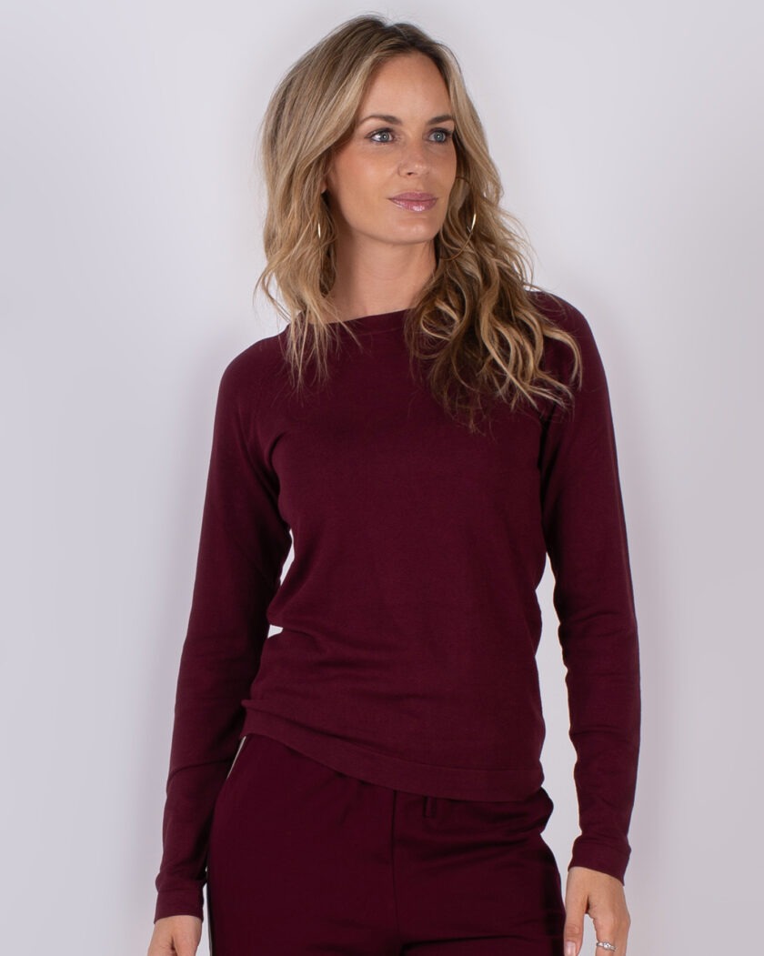 Vrouw draagt een bordeauxrode trui met bijpassende broek uit Studio AW25-26 collectie.