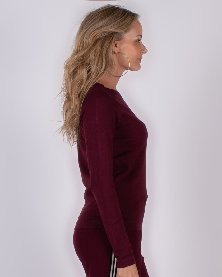 Vrouw in profiel draagt een bordeauxrood, aangesloten truitje en bijpassende broek uit de Studio AW25-26 collectie.