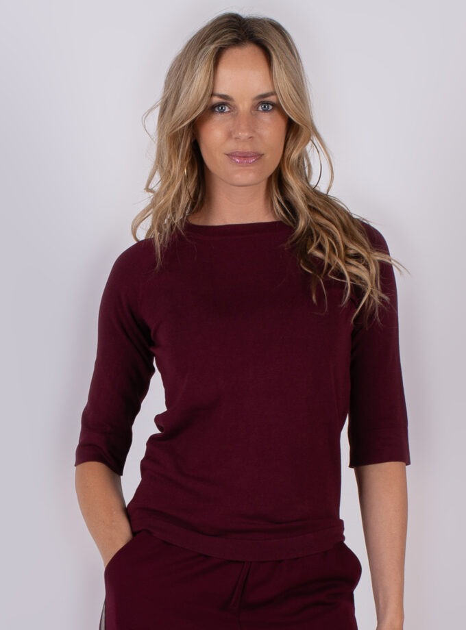 Vrouw poseert in een bordeauxrode top met driekwartsmouwen uit de Studio AW25-26 collectie.