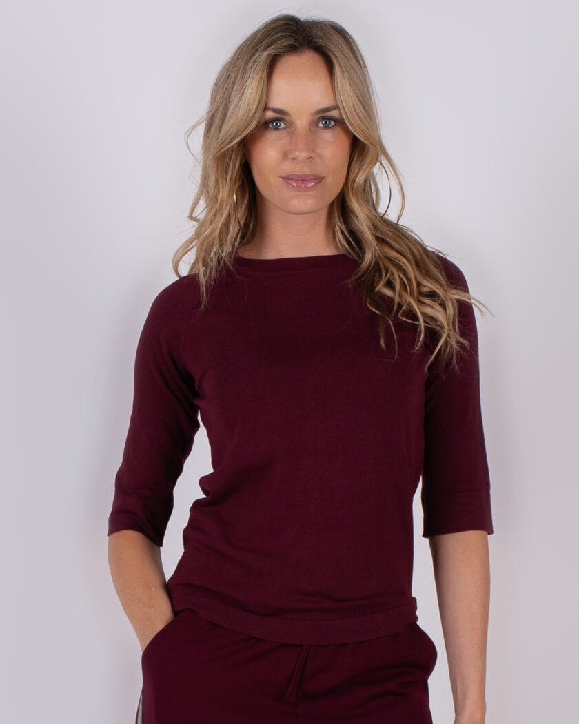 Vrouw poseert in een bordeauxrode top met driekwartsmouwen uit de Studio AW25-26 collectie.