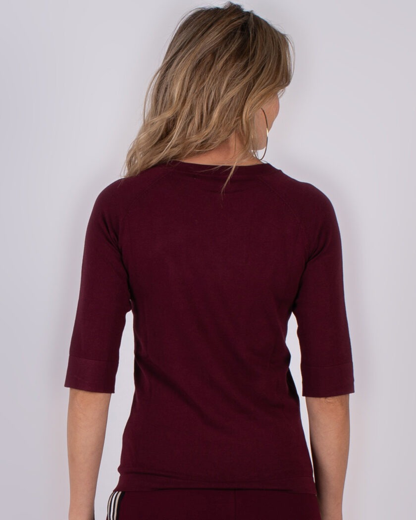 Vrouw van achteren gefotografeerd in een bordeauxrode top met driekwartsmouwen uit de Studio AW25-26 collectie.