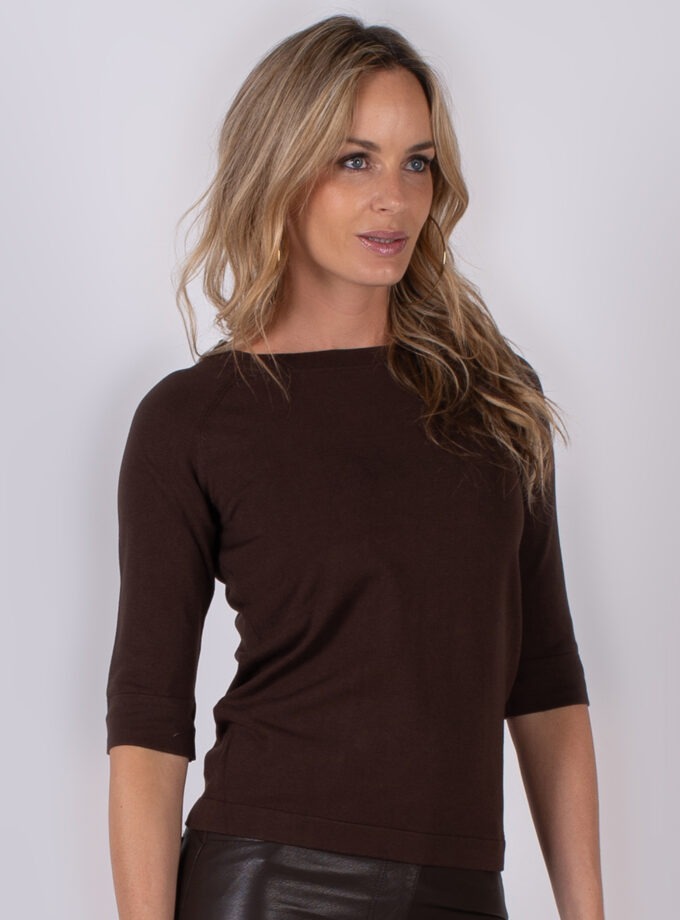 Vrouw met lang blond haar draagt een donkerbruine top met driekwartmouwen uit de Studio AW25-26 collectie.