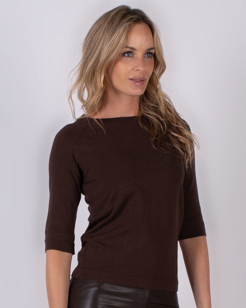Vrouw met lang blond haar draagt een donkerbruine top met driekwartmouwen uit de Studio AW25-26 collectie.