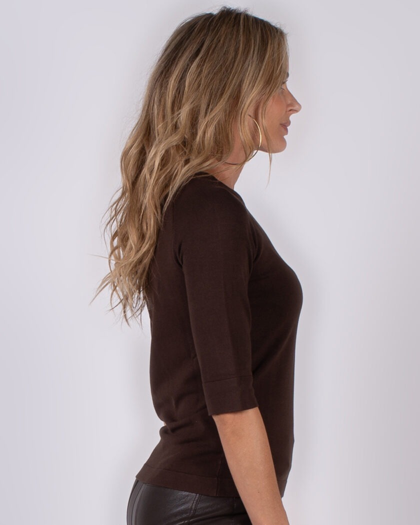 Vrouw in profiel met lang golvend haar draagt een donkerbruine top met driekwartsmouwen.
