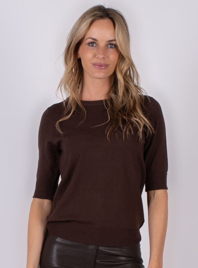 Vrouw draagt een donkerbruine top met halve mouwen uit de Studio AW25-26 collectie.