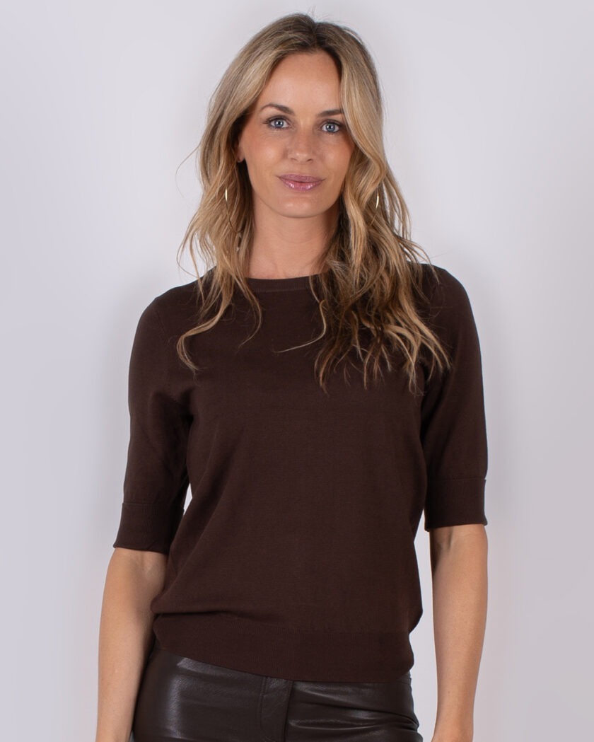 Vrouw draagt een donkerbruine top met halve mouwen uit de Studio AW25-26 collectie.