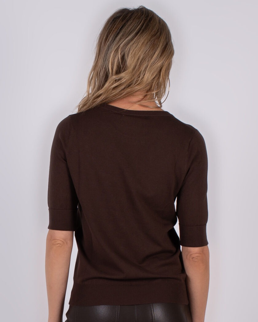Vrouw van achteren gezien die een donkerbruine trui met halve mouwen draagt uit de Studio AW25-26 collectie.
