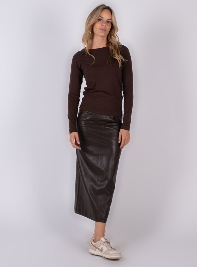Vrouw gekleed in een donkerbruine trui en een lange, glanzende lederen rok met beige sneakers.